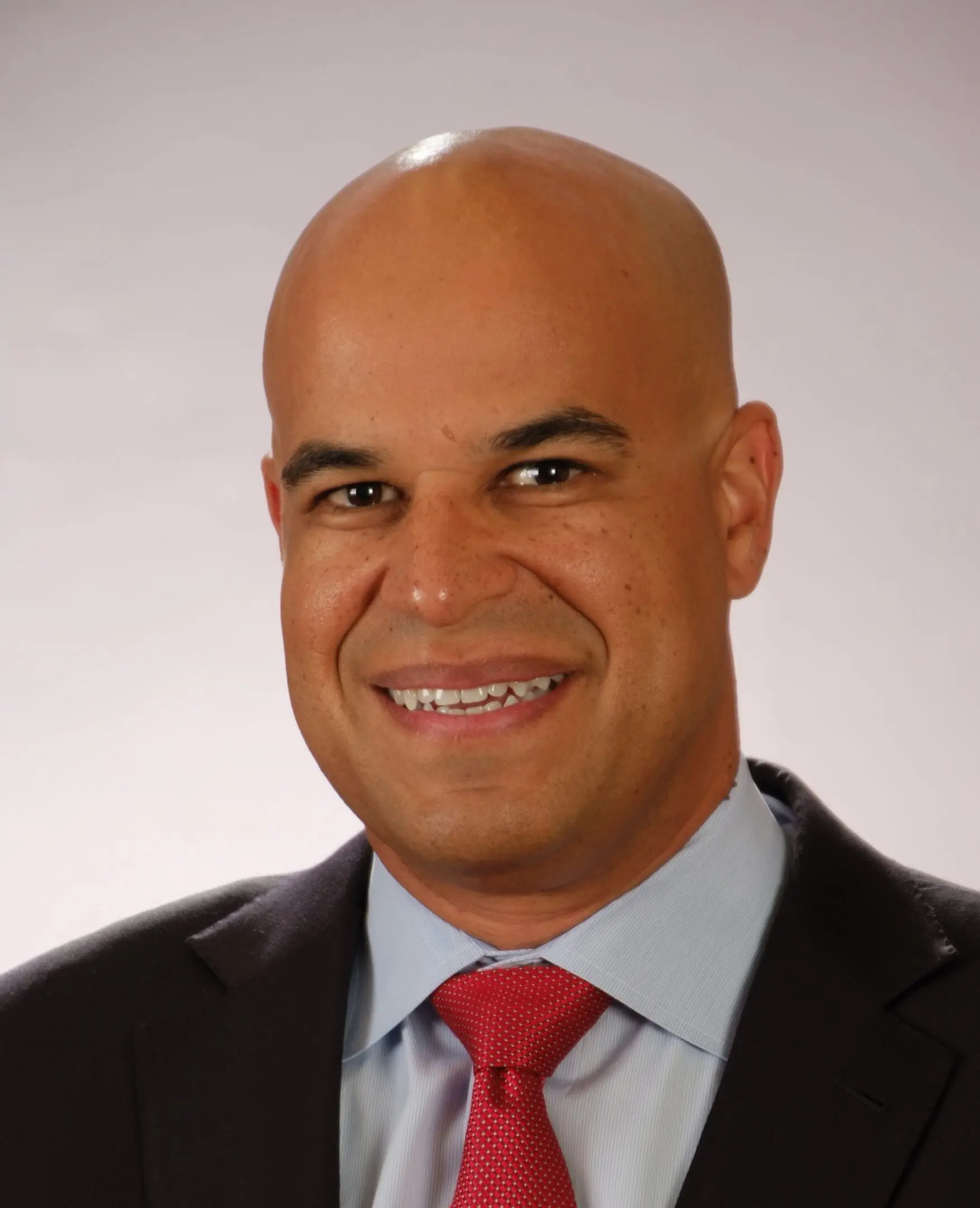 Professional headshot of a smiling bald man in a suit and red tie.