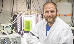 Scientist in lab coat near glowing equipment.