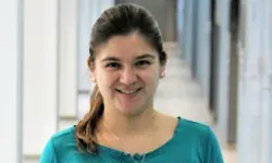 Smiling woman in a hallway, wearing teal.