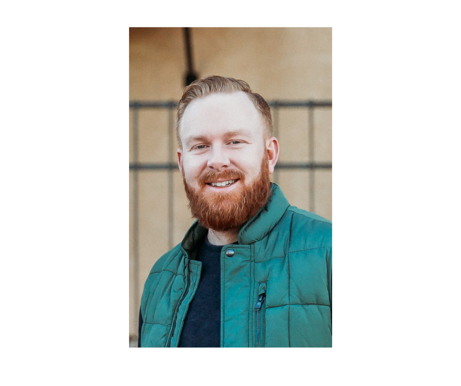 Smiling man with a beard wearing a green jacket outdoors.