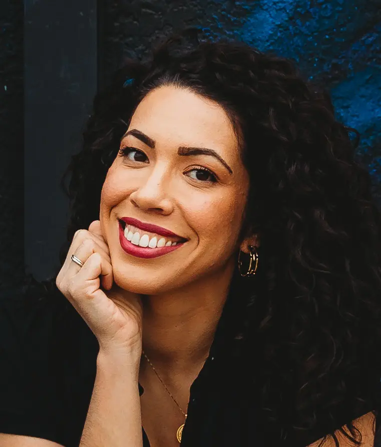 Smiling woman with curly hair resting her chin on her hand.