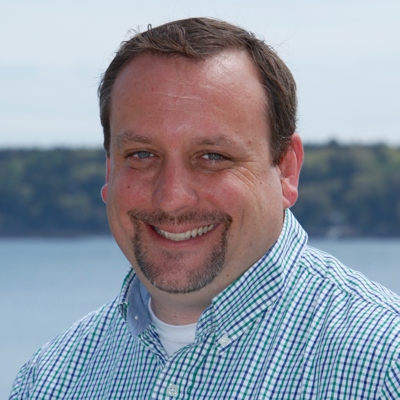 Smiling man in a checkered shirt outdoors by water.