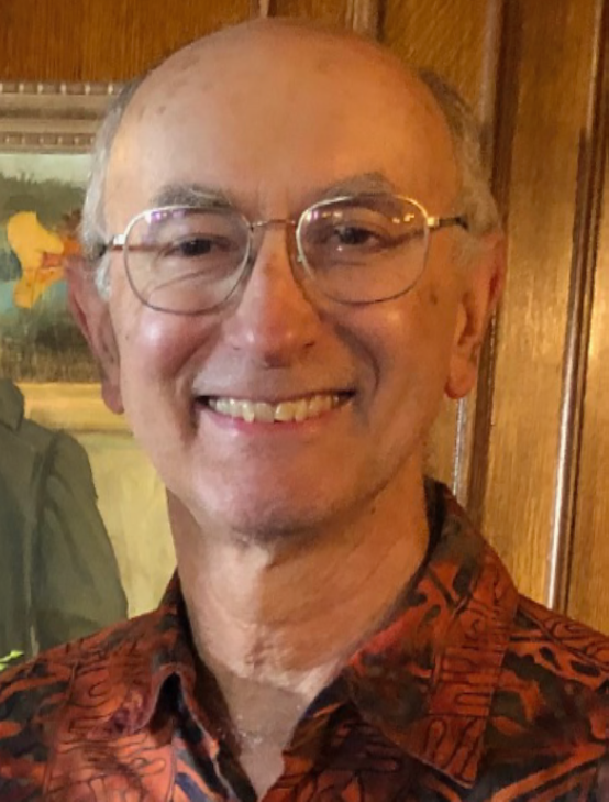 Smiling elderly man wearing glasses and a patterned shirt.
