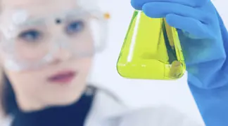Scientist examining yellow liquid in flask.