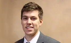 Man in suit smiling against beige background.