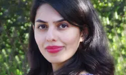 Woman smiling with greenery in background.