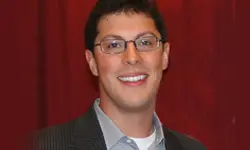 Smiling person wearing glasses against red background.