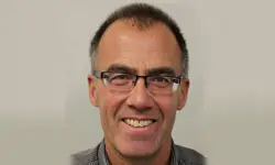 Smiling man wearing glasses, neutral background.