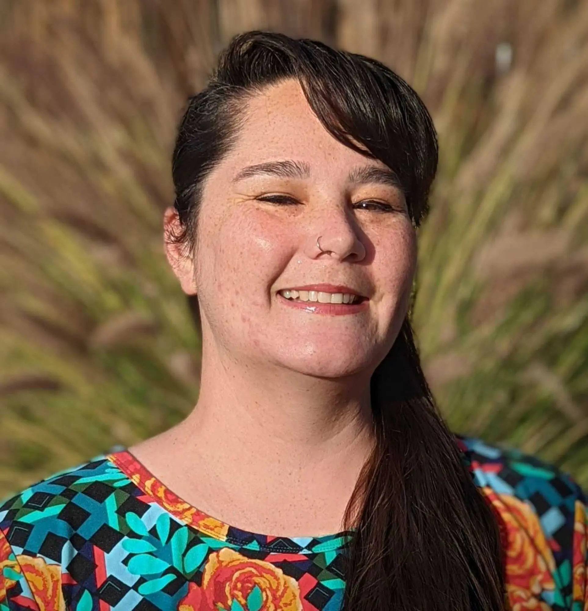 Smiling woman with dark hair and colorful floral shirt outdoors.