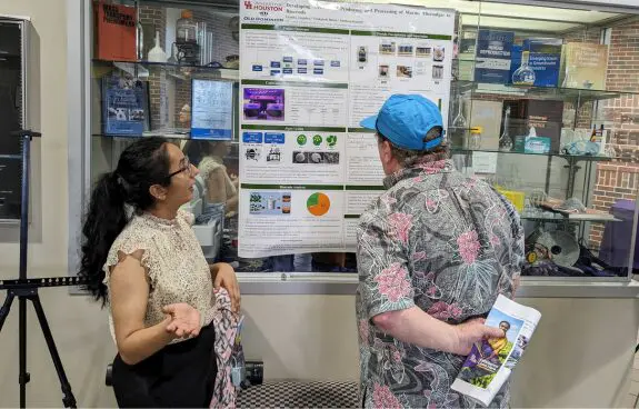 Two people discussing a scientific poster presentation indoors.