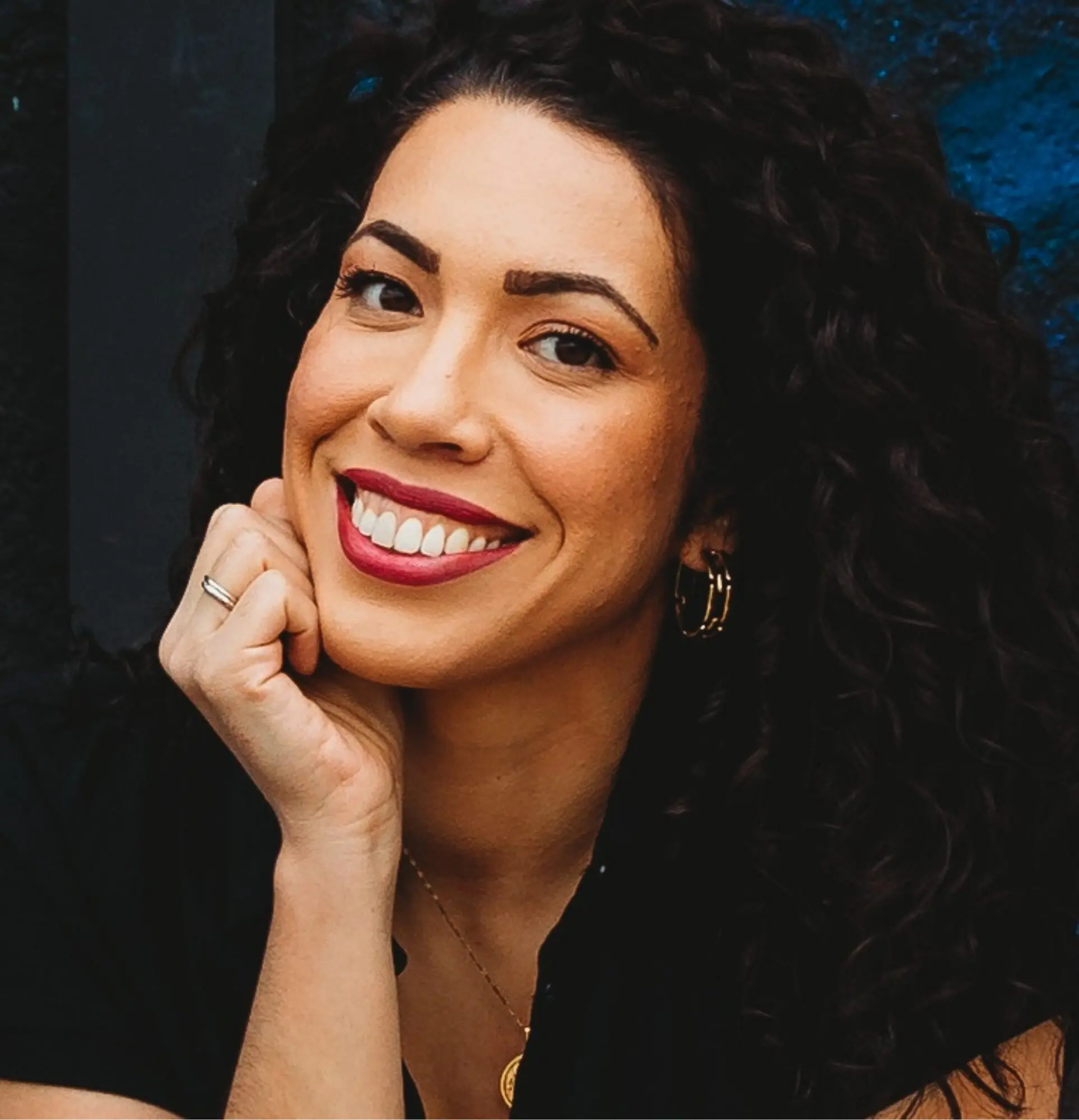 Smiling woman with curly hair resting her chin on her hand.