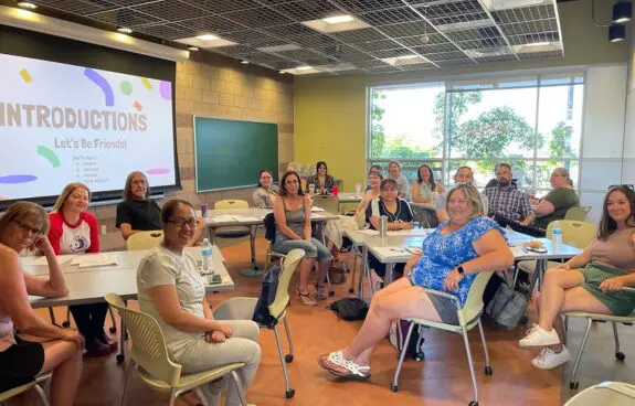A group of students and a teacher in a brightly lit classroom.