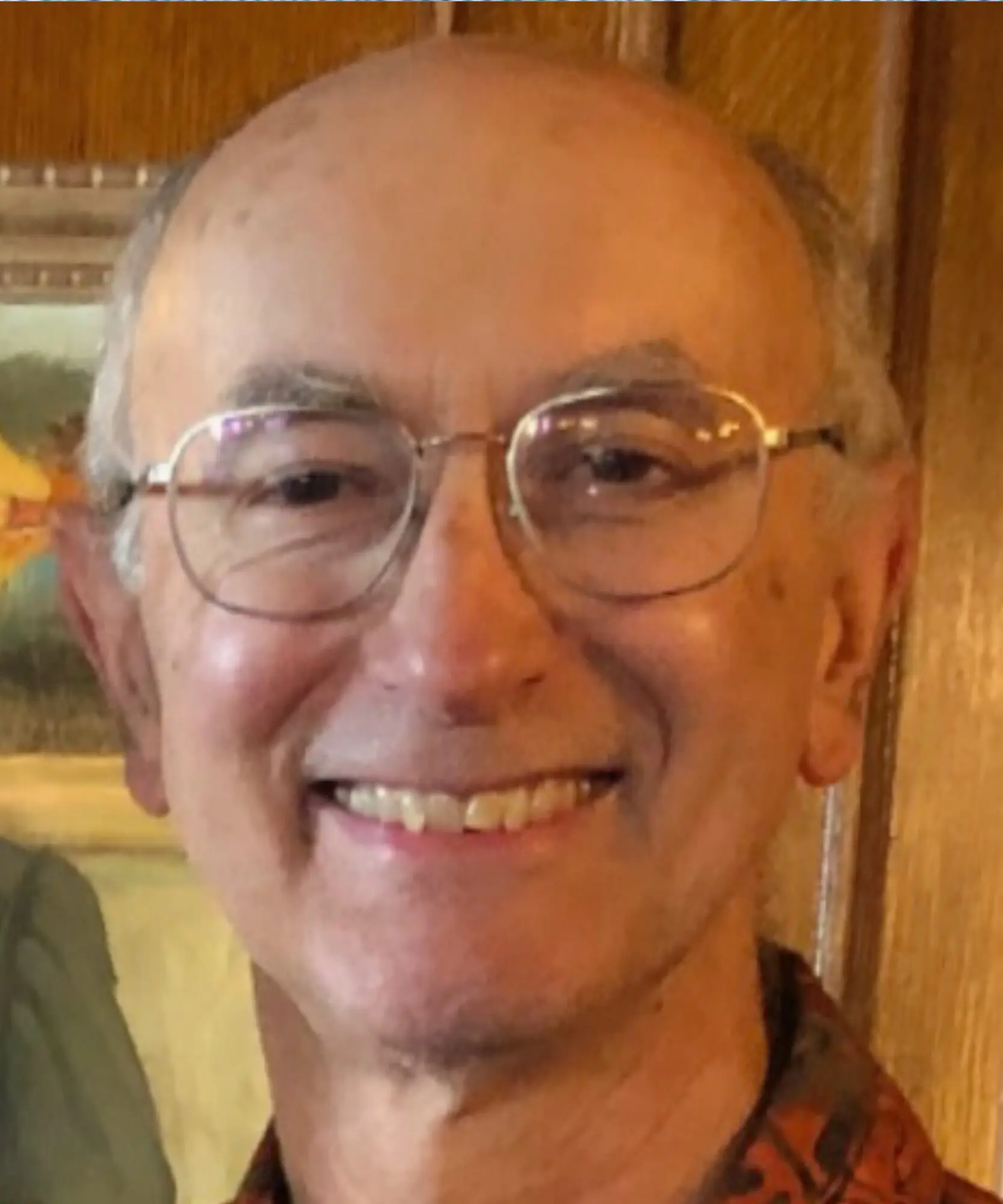 Elderly man wearing glasses smiling warmly.