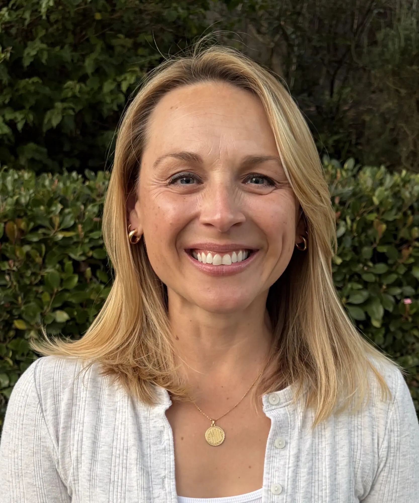 Smiling woman outdoors with greenery background.