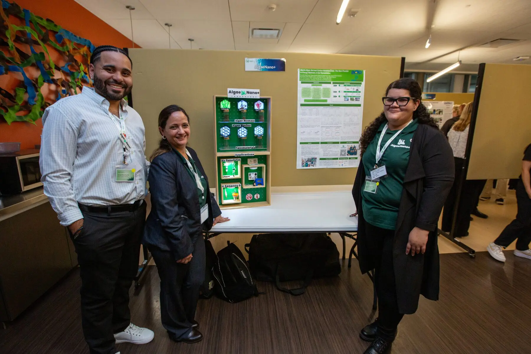 Three people standing by a science project display board in a classroom.