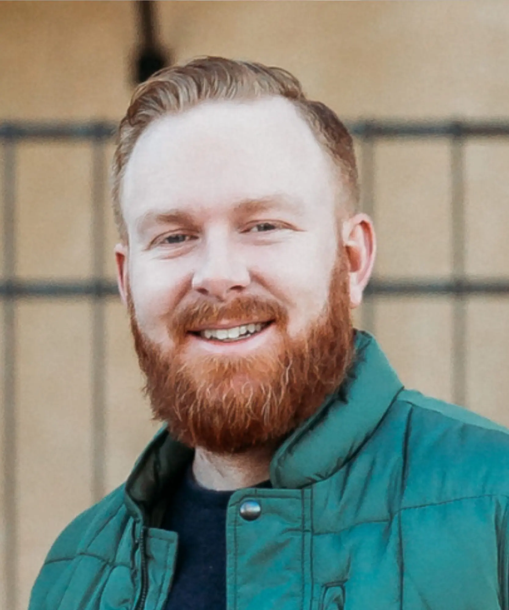 Smiling man with red hair and beard in green jacket.