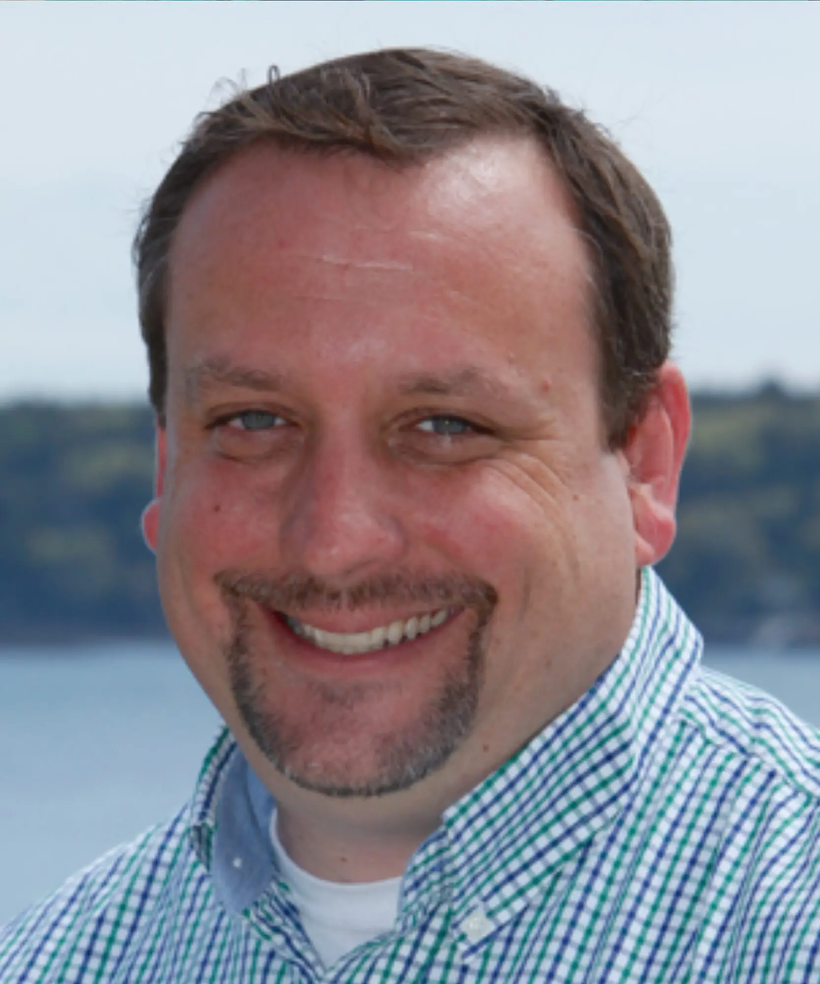 Smiling man outdoors with a scenic background.