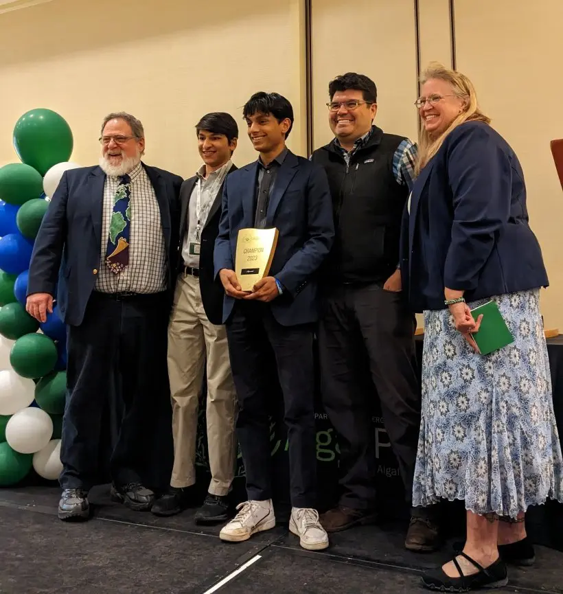 A group of five people posing with an award plaque, smiling.