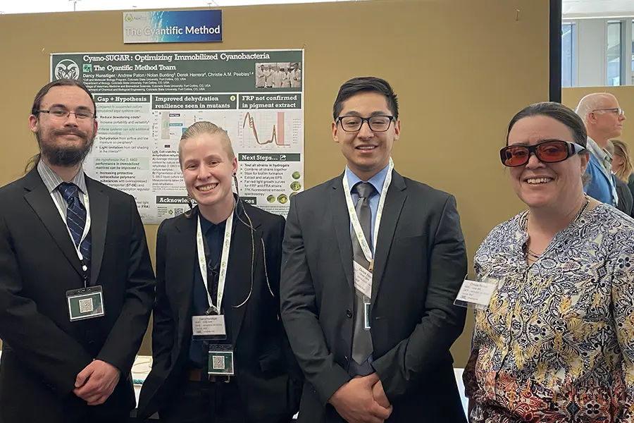 Four professionals standing in front of a research poster at a conference.