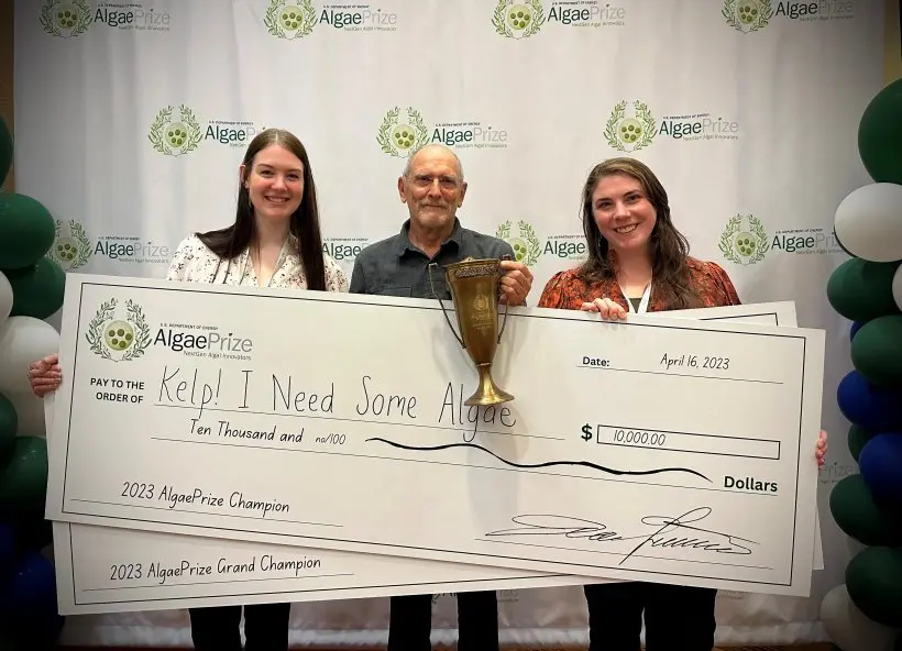 Three people holding a large check and trophy at an awards event.