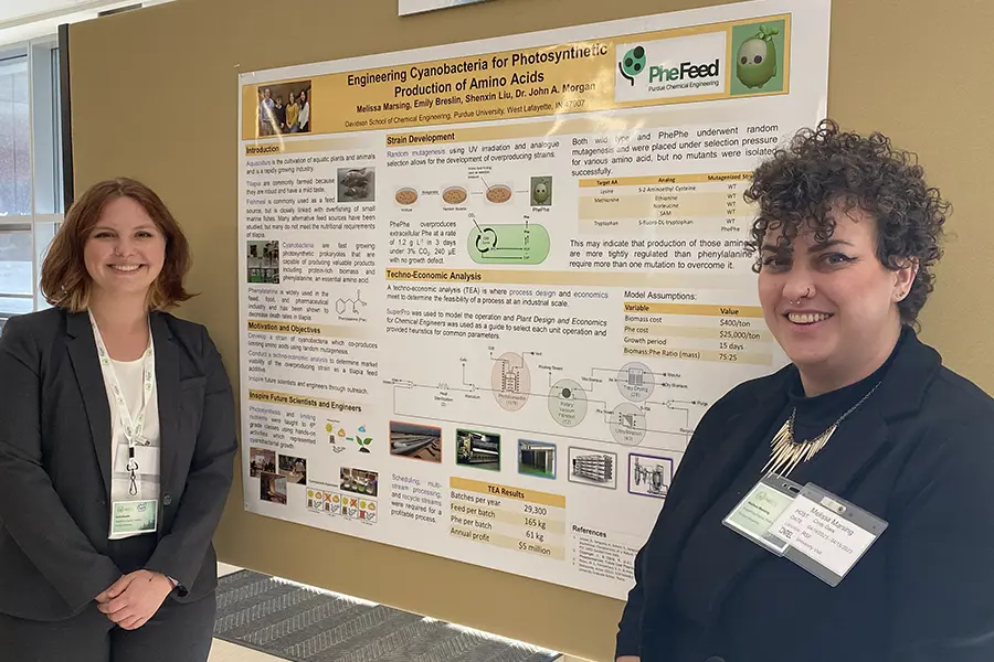 Two women standing beside a scientific research poster at a conference.