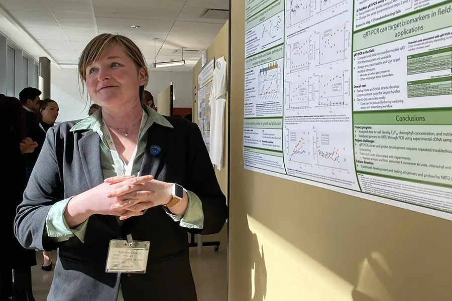 Woman standing near a wall with charts or documents posted on it.