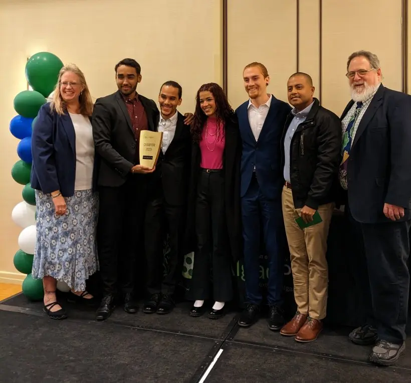 A group of seven people posing with an award on stage.