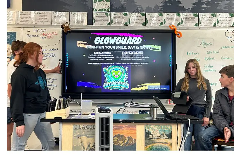 Two presenters explain GlowGuard at a workshop with a screen and posters behind them.