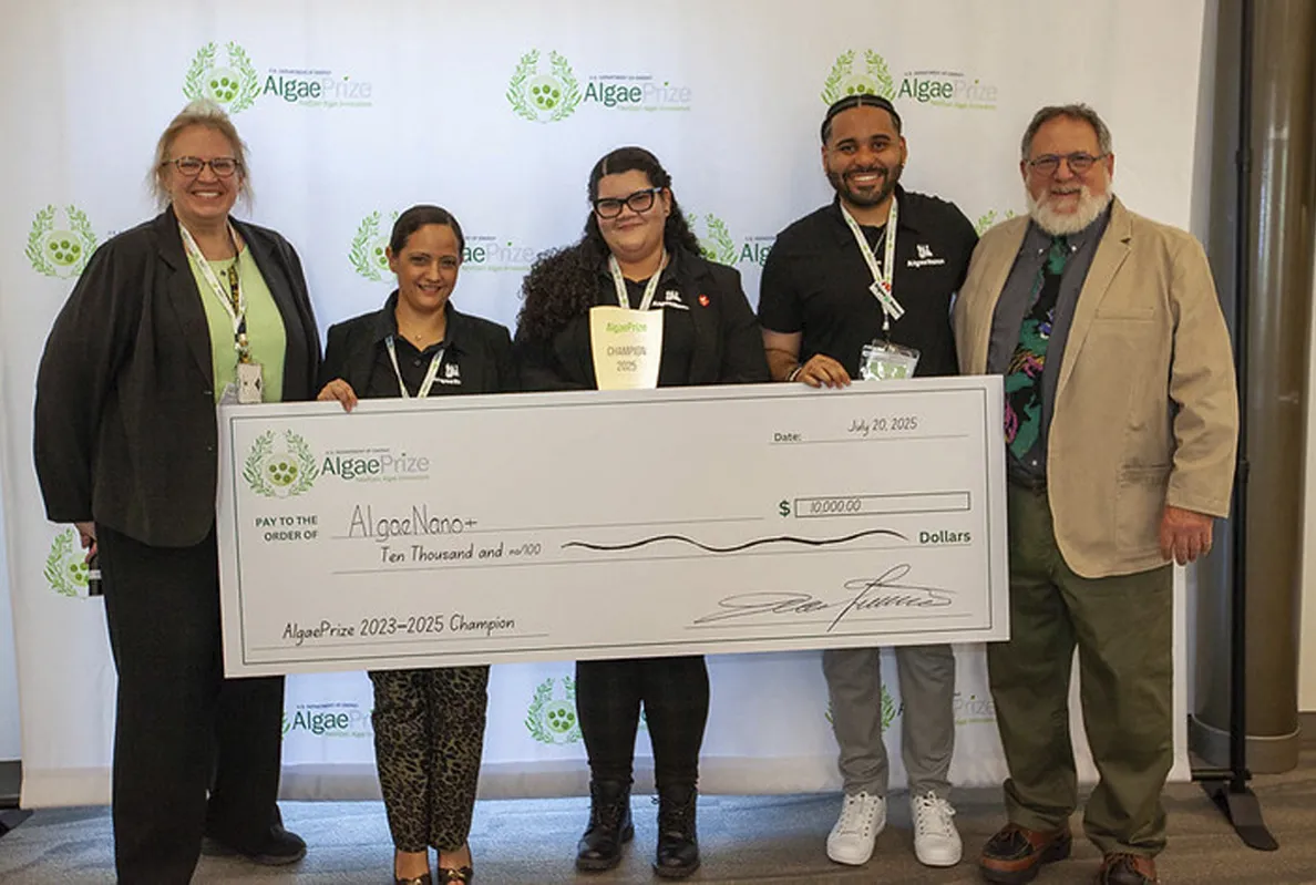 Group celebrating with a large check and trophy at an event.