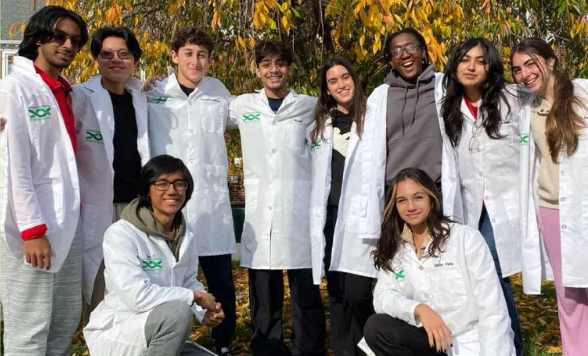 Group of young scientists in white lab coats smiling outdoors.