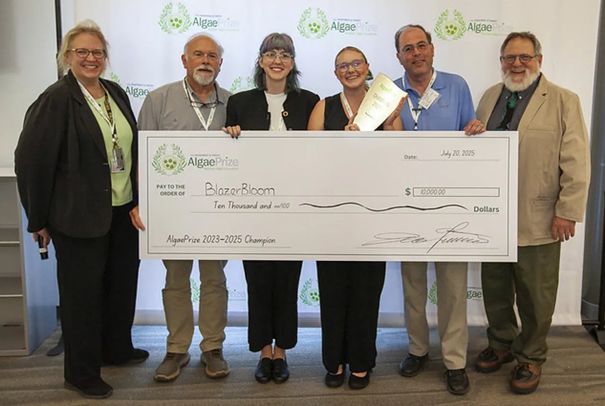 Group of six people holding a large donation check indoors.