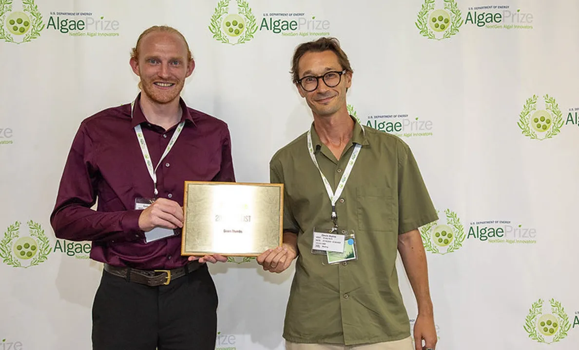 Two men holding a certificate at an event with Algae branding.