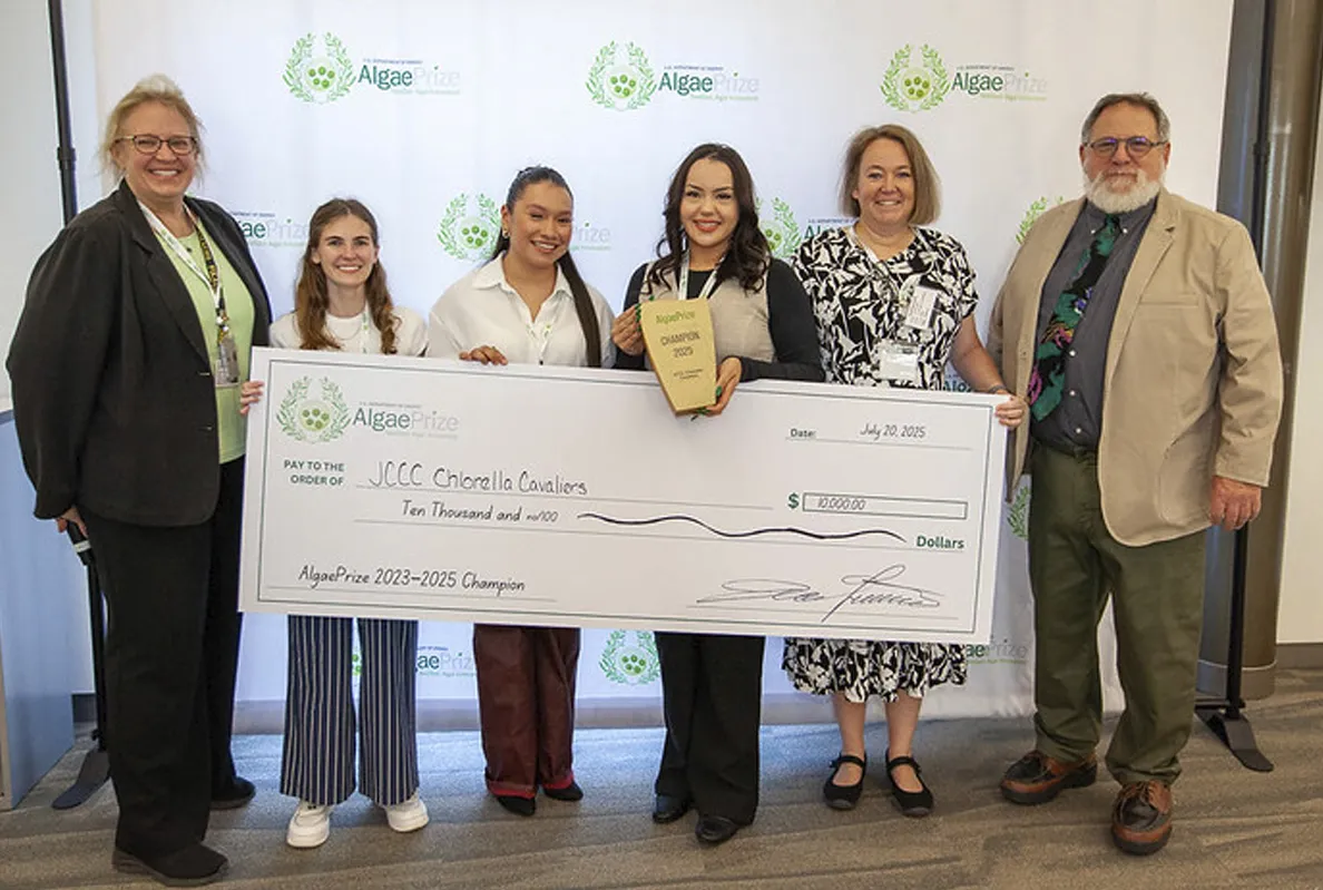 Group of women holding an award and a large check at a ceremony.