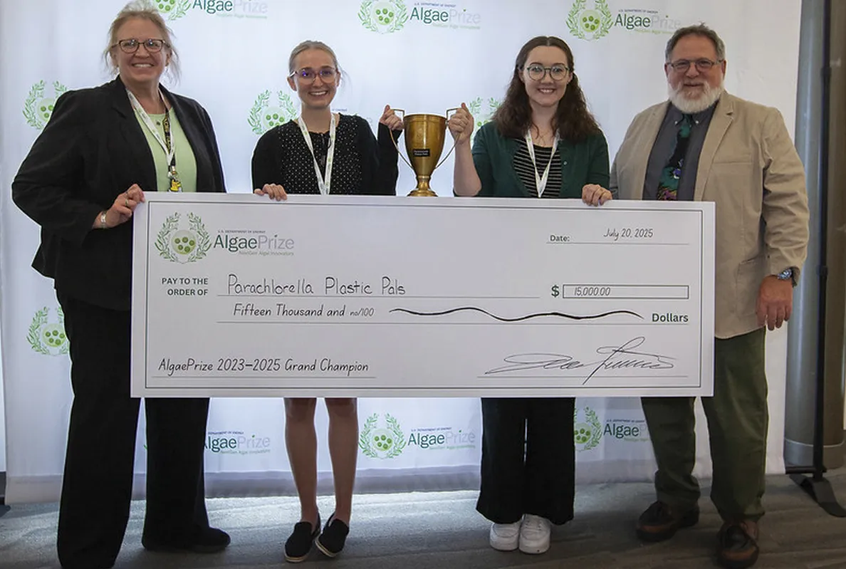 Four people holding a large check and trophy at an event.