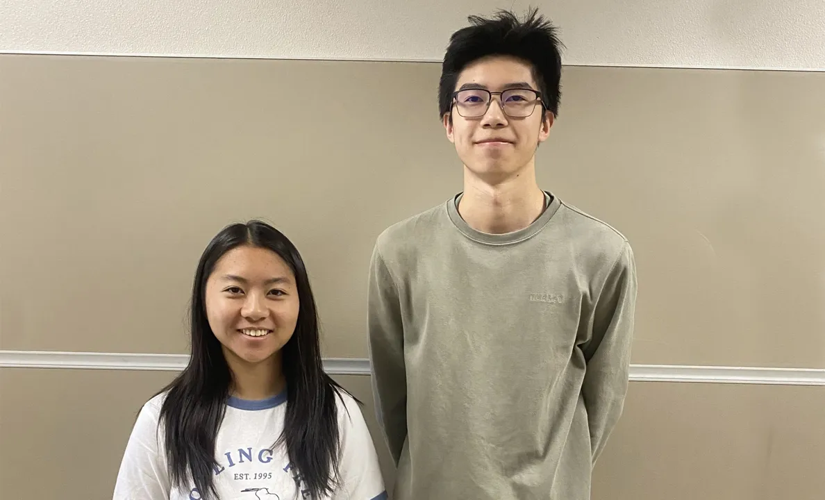 A young man and woman standing side by side indoors, smiling.